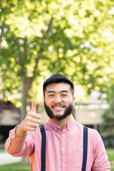 Vertical photo of an asian man in casual clothes gesturing being well with the hand in a park