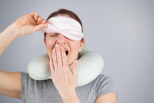 Caucasian woman yawns with travel pillow and sleep mask on white background