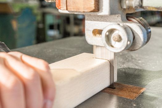 Hand of crop anonymous woodworker cutting wooden plank with professional metal band saw while working in light joinery with special equipment