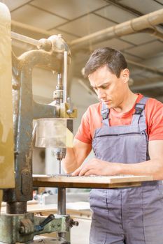 Concentrated male master in uniform drilling steel plank on professional metal machine while working in light joinery with special equipment