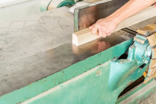 Hand of crop unrecognizable carpenter trimming wooden board while working at metal woodworking planer in professional light joinery during workday