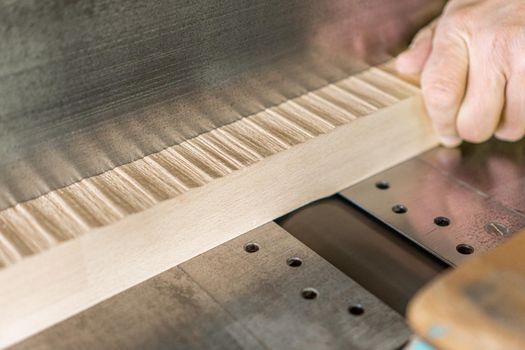 Hand of crop anonymous woodworker trimming wooden plank while working on professional metal woodworking planer in light carpentry during workday