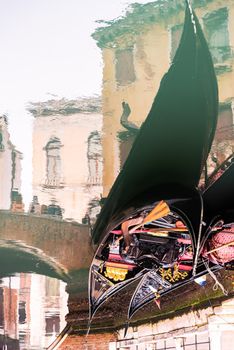 Upside down reflection of traditional Italian gondolas on rippling waterway among old stone buildings in Venice