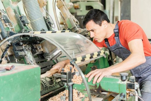 Side view of concentrated male carpenter in workwear shaping wooden detail on special equipment in professional workshop