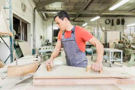 Side view of busy master in workwear shaping large piece of wood while working in professional joinery