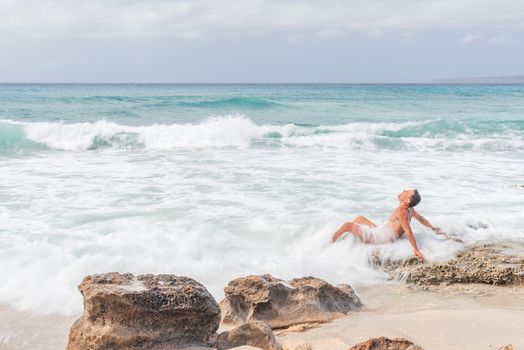 Side view of naked man leaning back and enjoying foamy waves of clean sea while spending time on beach on sunny day on Formentera island, Spain