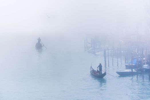 Distant unrecognizable gondolier carrying tourists in wooden boats on rippling canal water in hazy day in Venice