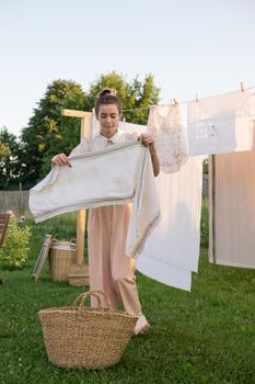 Laundry day. A woman hangs linen and towels on a tree in the courtyard of a village house. Summer cottage concept.