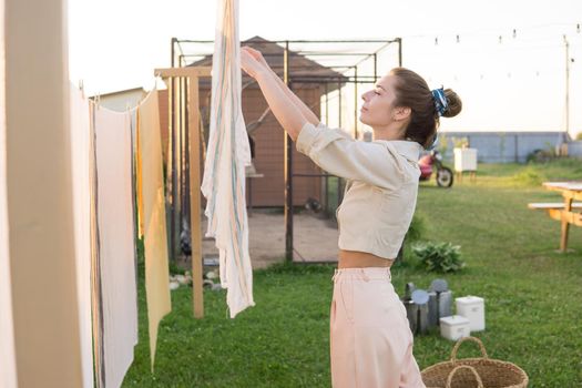 Laundry day. A woman hangs linen and towels on a tree in the courtyard of a village house. Summer cottage concept.