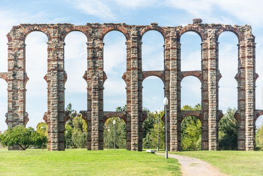 Old stone Miraculous aqueduct with columns over green meadow and verdant trees in sunny day in Spain