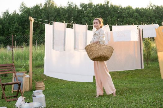 Laundry day. A woman hangs linen and towels on a tree in the courtyard of a village house. Summer cottage concept.