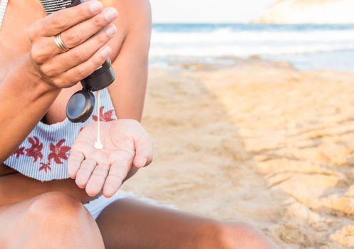 Crop unrecognizable female in swimwear applying sunscreen while resting on sandy beach near waving sea during summer vacation in Spain