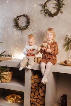 Little brother and sister play on Christmas eve in a beautiful house decorated for the New Year holidays. Children are playing with a Christmas gift. Scandinavian-style interior with live fir trees and a wooden staircase.