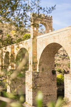 Roman arched bridge with stone walls located near green trees on sunny day in Spain