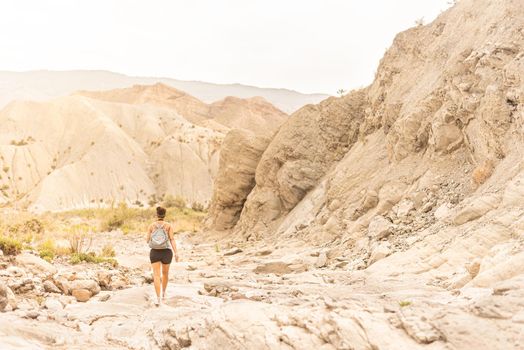 Back view of anonymous female tourist with backpack exploring sandy mountainous terrain in Tabernas desert