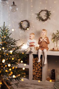 Little brother and sister play on Christmas eve in a beautiful house decorated for the New Year holidays. Children are playing with a Christmas gift. Scandinavian-style interior with live fir trees and a wooden staircase.