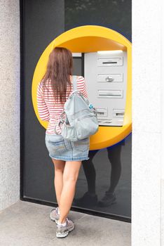 Back full body view of unrecognizable woman with backpack using ATM terminal in city while traveling in summer day