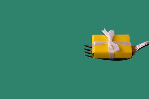 yellow gift with white ribbon lies on fork on green background. holiday, christmas or birthday concept. copy space,