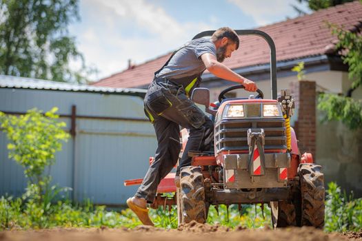 A man on a mini-tractor levels a plot of land, loosens the soil.