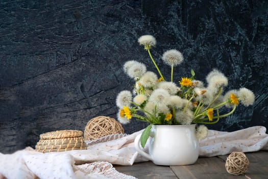 air bouquet of dandelions in a white mug on a black textured background. soft focus