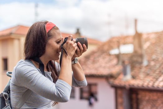 Side view of focused Hispanic woman with backpack taking photo of old town using photo camera while traveling in Spain during vacation in daytime