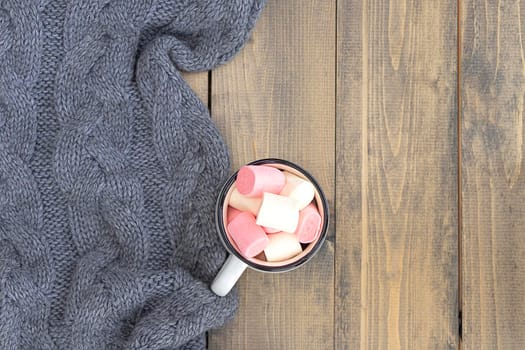 flat lay with mug full of marshmallows on wooden table with knitted warm gray plaid. autumn or winter concept. copy space. soft focus