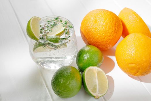 Alcoholic cocktail in a glass on a light background with lime and thyme and orange.