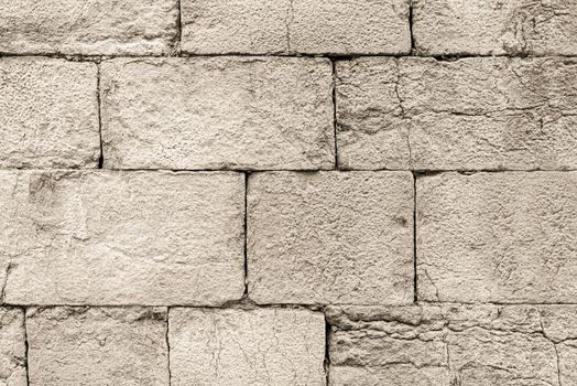 Textured backdrop of rough surface of aged gray stone brick wall with cracks and holes in daylight