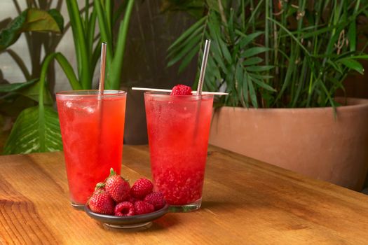 tropical red fruit drink on wooden table with plant background. strawberries, raspberries, red color drink