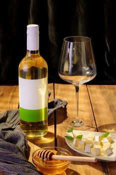 A bottle of white wine with an empty glass, sliced cheese and honey