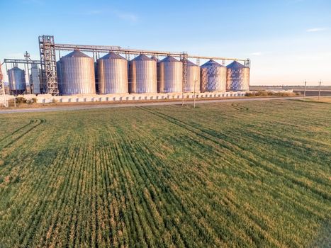 Grain elevator. Metal grain elevator in agricultural zone. Agriculture storage for harvest. Grain silos on green nature background. Exterior of agricultural factory