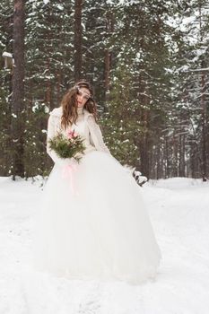 Beautiful bride in a white dress with a bouquet in a snow-covered winter forest. Portrait of the bride in nature.