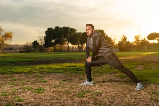 Full body of bearded male runner in sportswear doing lunge exercise during outdoor training in park at sundown