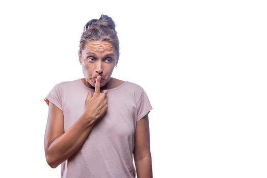 Front view of a confused and guilty-looking adult woman looking away covering her mouth with a finger on a white background with copy space.