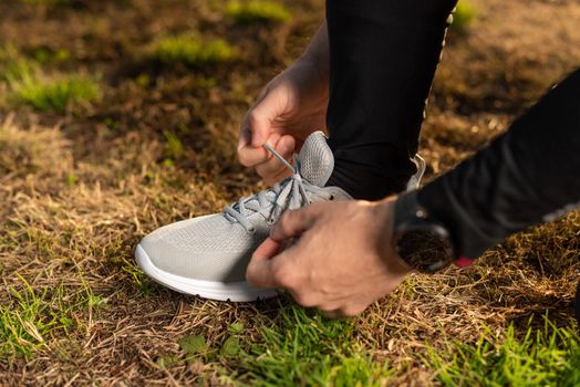 High angle of crop anonymous male runner tying laces of sport footwear on grassy ground during outdoor fitness workout