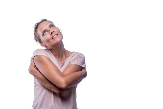 Front view of a green-eyed tender romantic woman embraces own body, hugs herself, looking up on a white background with copy space. Concept i love myself.