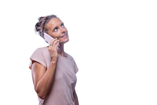 Front view of a green-eyed woman speaking with her phone while looking up on a white background with copy space.