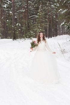 Beautiful bride in a white dress with a bouquet in a snow-covered winter forest. Portrait of the bride in nature.