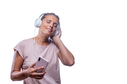 Front view of a pleased adult woman listening music with her headphones and smartphone with her eyes closed on a white background with copy space.