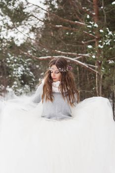 Beautiful bride in a white dress with a bouquet in a snow-covered winter forest. Portrait of the bride in nature.