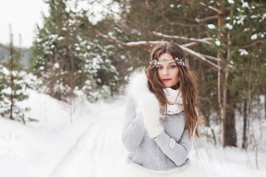Beautiful bride in a white dress with a bouquet in a snow-covered winter forest. Portrait of the bride in nature.