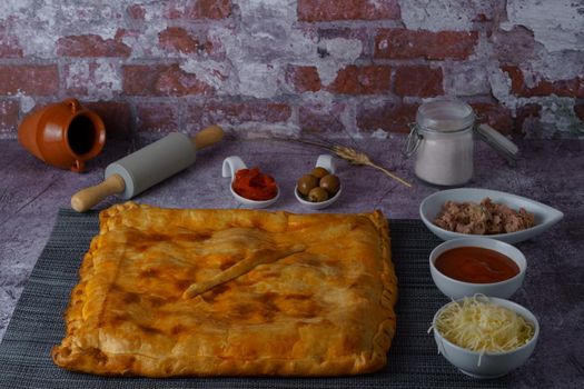 tuna empanada with all the ingredients separated in ceramic containers in the bottom of a red brick wall