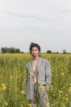 An Asian model poses in a field of yellow flowers for a clothing brand, polyethylene is the main props for a photo shoot. The concept of manufacturing clothing from recycled plastic. A woman in a pantsuit is standing on a plastic bag.