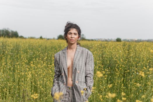 An Asian model poses in a field of yellow flowers for a clothing brand, polyethylene is the main props for a photo shoot. The concept of manufacturing clothing from recycled plastic. A woman in a pantsuit is standing on a plastic bag.