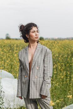 An Asian model poses in a field of yellow flowers for a clothing brand, polyethylene is the main props for a photo shoot. The concept of manufacturing clothing from recycled plastic. A woman in a pantsuit is standing on a plastic bag.