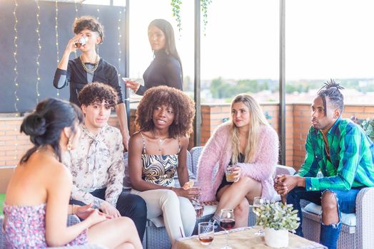 Multi-ethnic friends chatting on a terrace while having a drink at daytime.