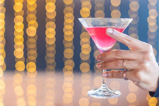 A hand holding a glass with a red cocktail on blurred background with copy space.