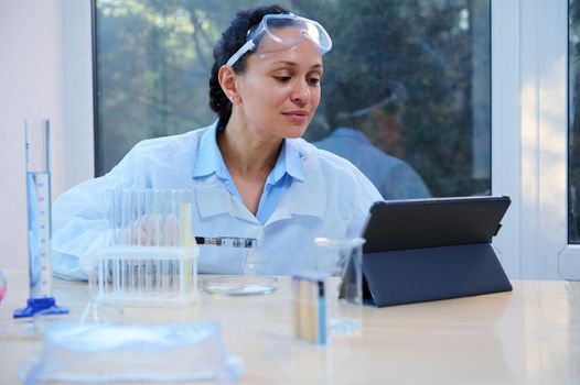 Pleasant middle-aged woman, Latin American female scientist pharmacologist conducting scientific experiments and analyzing the results on a digital tablet while working in a medical bio laboratory