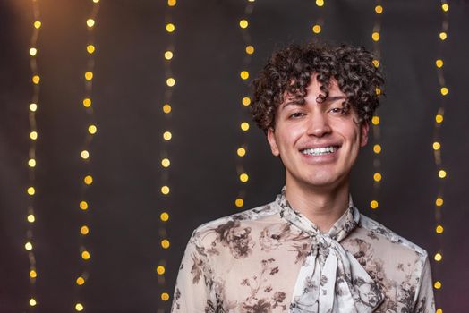 Portrait of young gay man looking at camera and smiling with a blurred light background in New Year's Eve with copy space