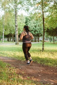 A charming brunette woman plus-size body positive practices sports in nature.